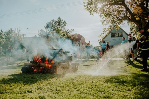 Firefighters spray water near a smoking outdoor fire as people watch