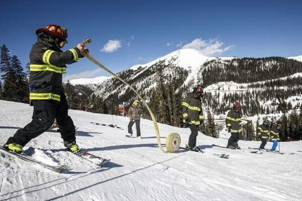 Firefighters carry a hose across a snowy mountain slope