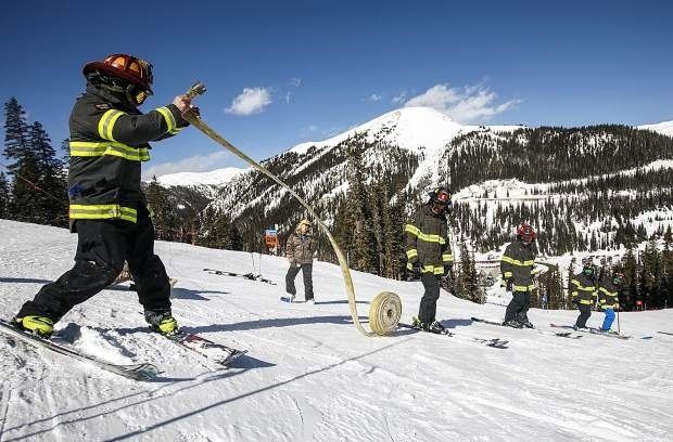 Firefighters carry a hose across a snowy mountain slope