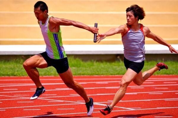 Two relay runners exchange a baton on a red track