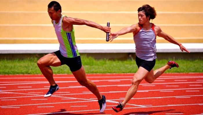 Two relay runners exchange a baton on a red track