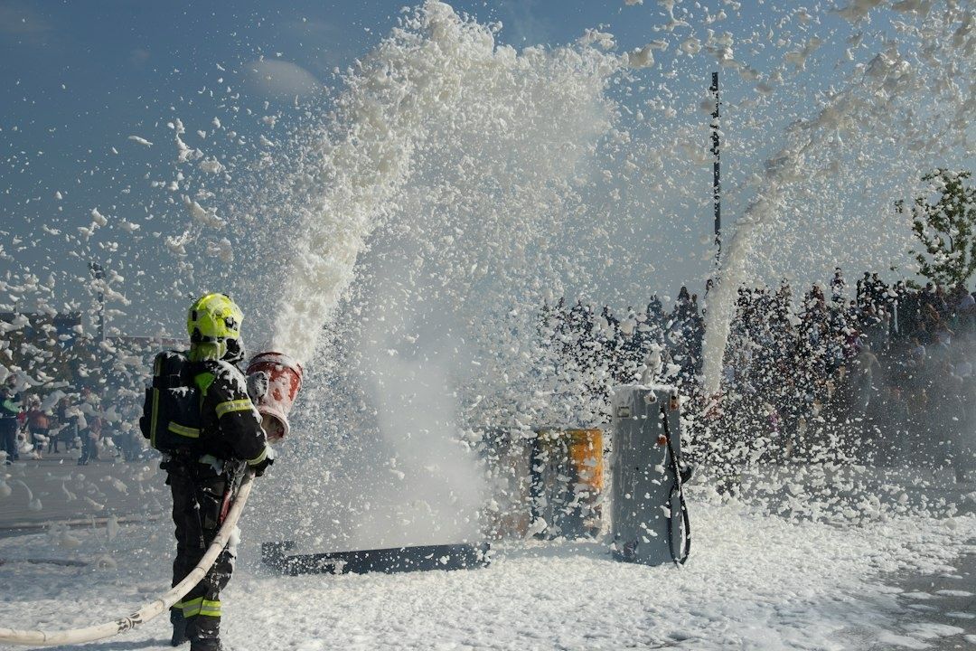 Firefighter operates a hose beside a portable pump amid spraying water