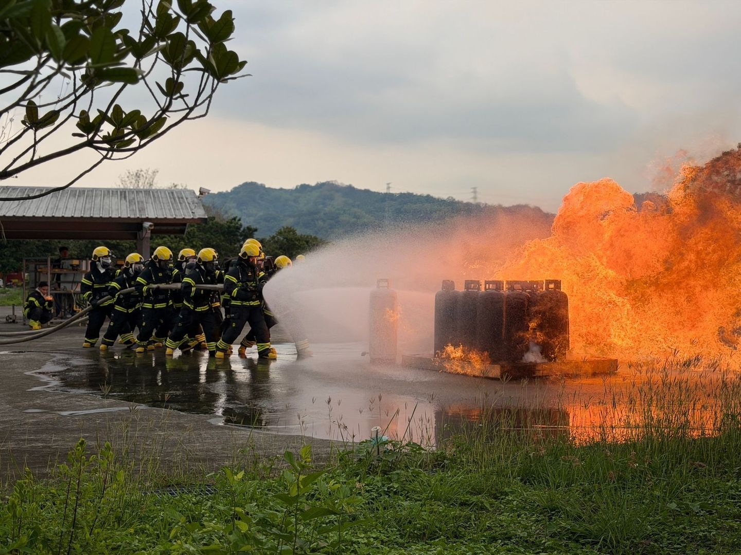 Firefighters practice a coordinated hose attack on a large outdoor fire