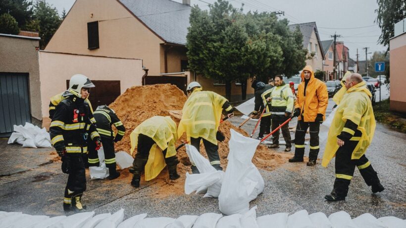 Firefighters and volunteers fill sandbags on a rainy residential street