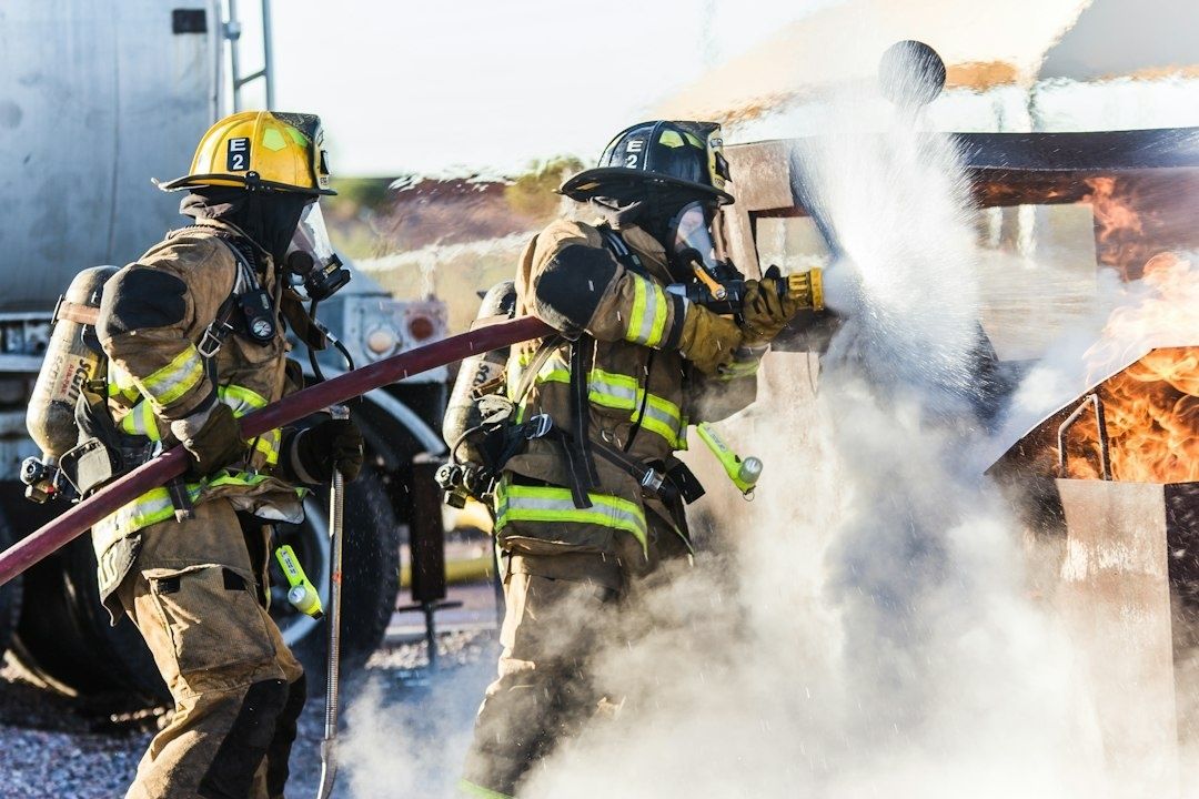 Two firefighters spray water on a burning training structure